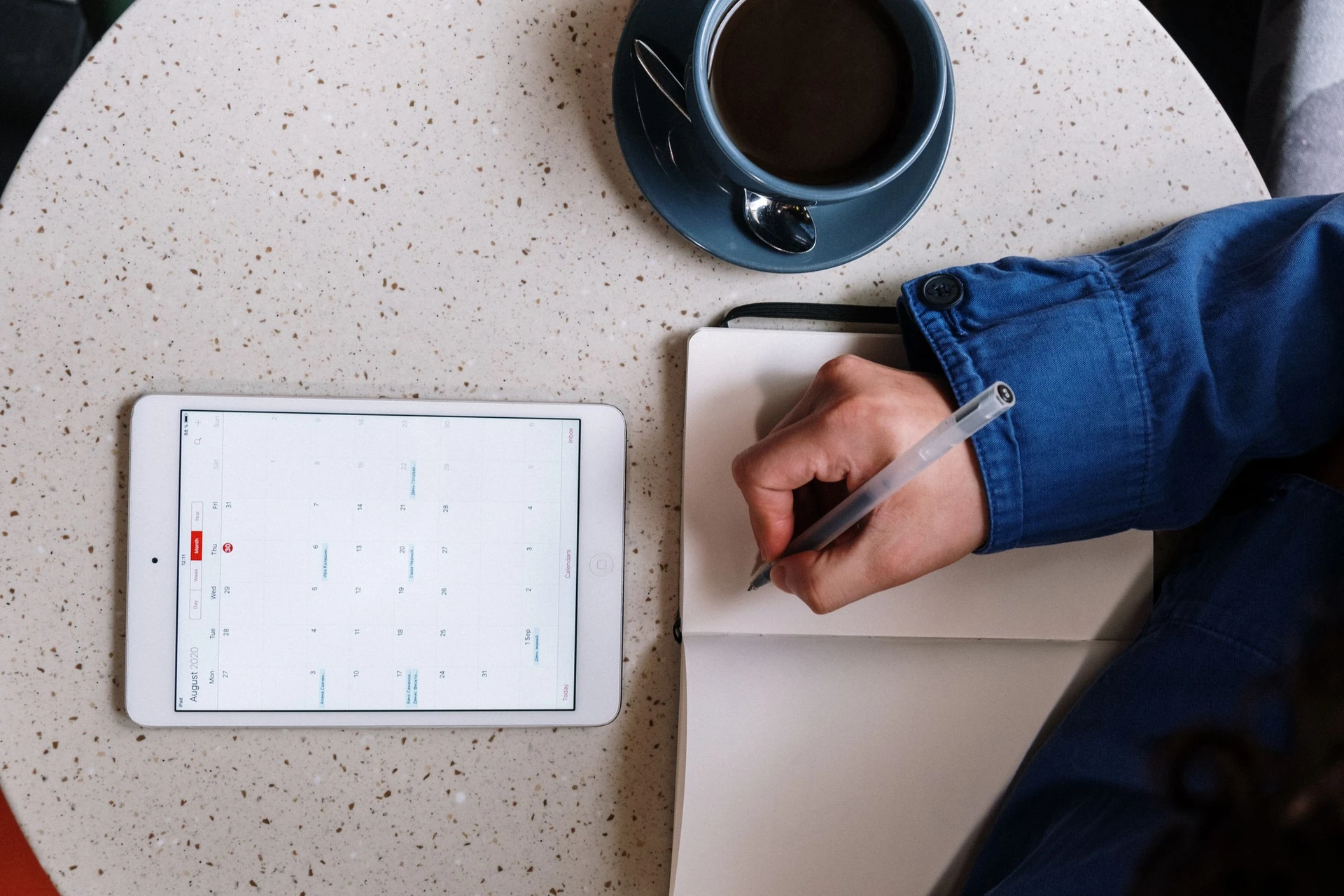 A person planning a schedule with a tablet calendar and notebook